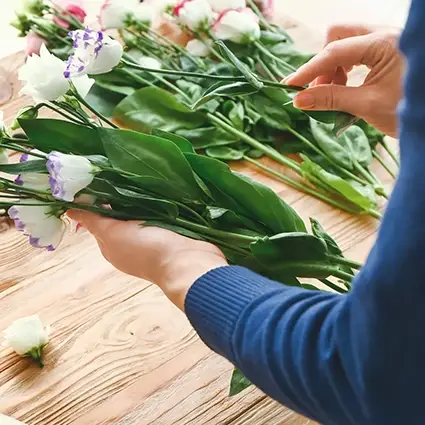 Persoon schikt bloemen voor een rouwboeket op een houten tafel